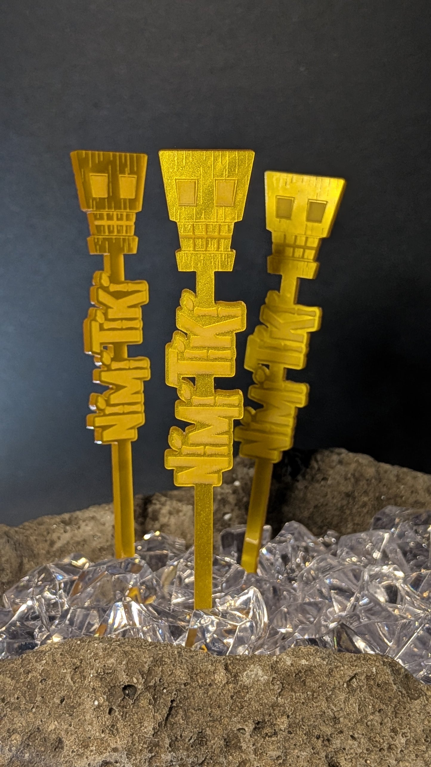 Three gold acrylic numbskull swizzle sticks in ice against a dark background