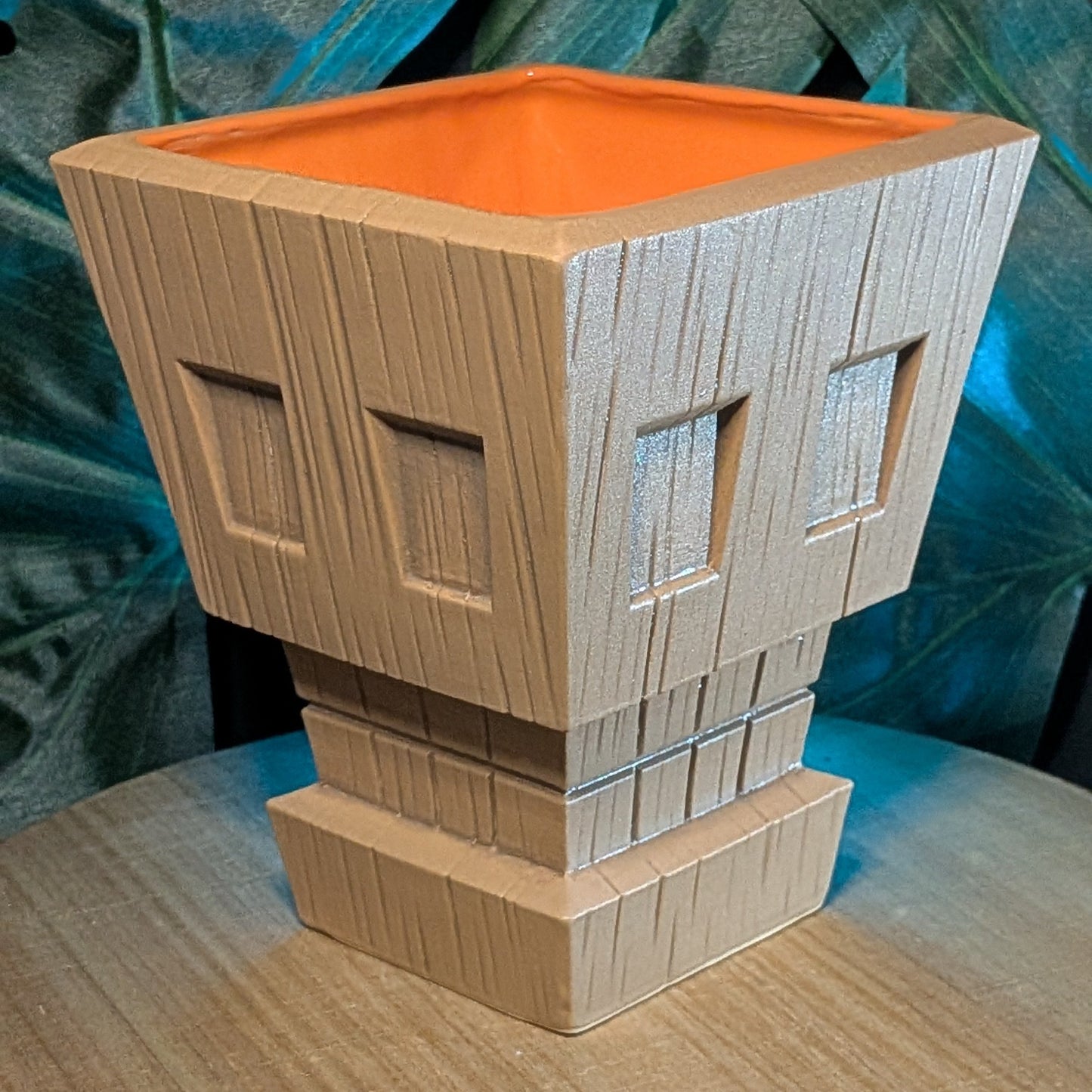 Wooden tiki mug shaped like a stylized skull with an orange interior against a green leafy background