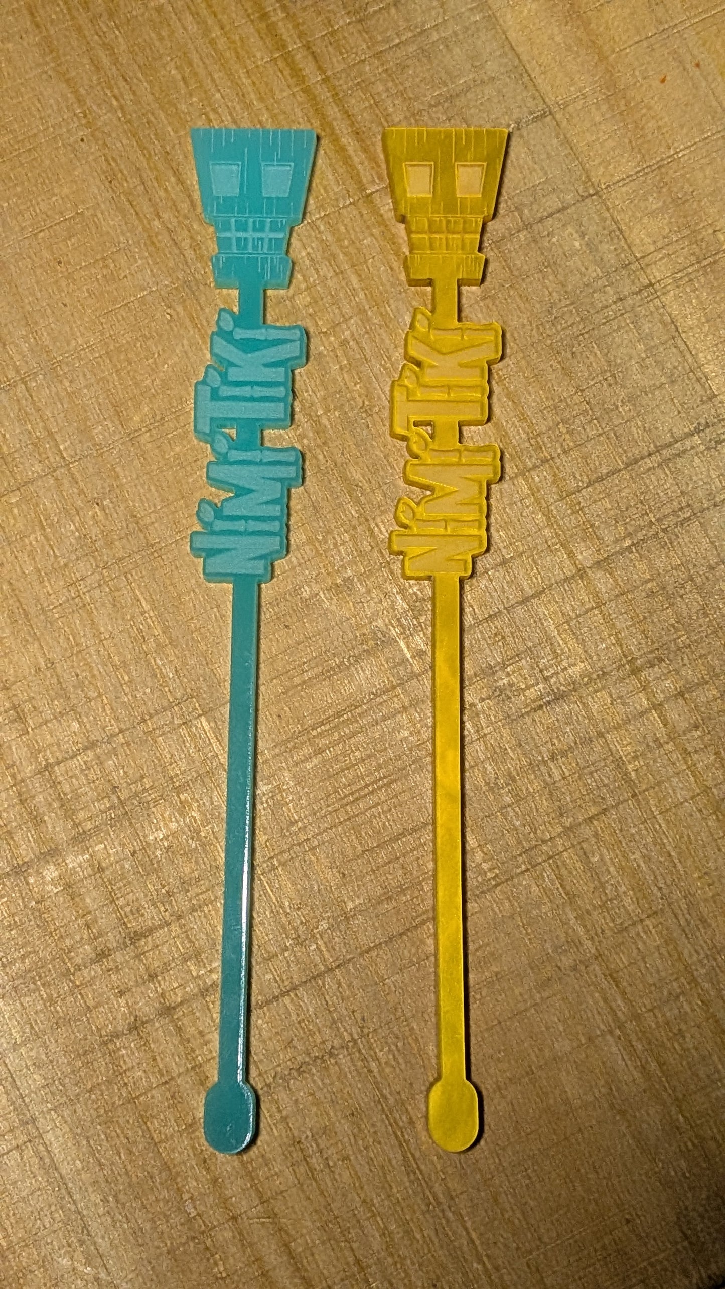Two plastic stir sticks, one blue and one yellow, on a wooden surface.
