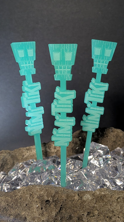 Three teal numbskull swizzles sticks in ice against a dark background
